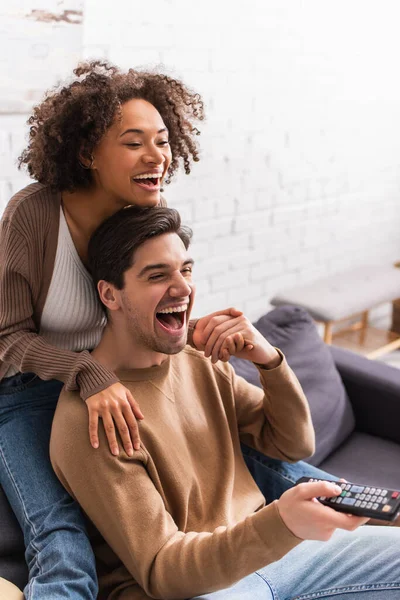 Smiling african american woman holding hand of boyfriend with remote controller on couch at home — Stock Photo