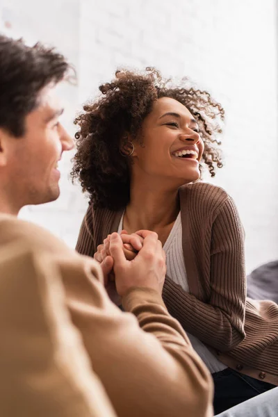 Smiling man holding hands of african american girlfriend at home — Stock Photo