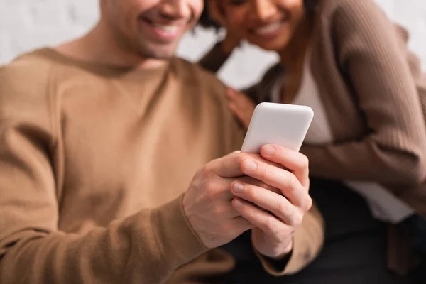 Vue recadrée d'un couple multiethnique utilisant un smartphone à la maison — Photo de stock