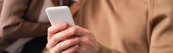 Ausgeschnittene Ansicht eines Mannes mit Smartphone in der Nähe einer afrikanisch-amerikanischen Freundin auf verschwommenem Hintergrund, Banner — Stockfoto