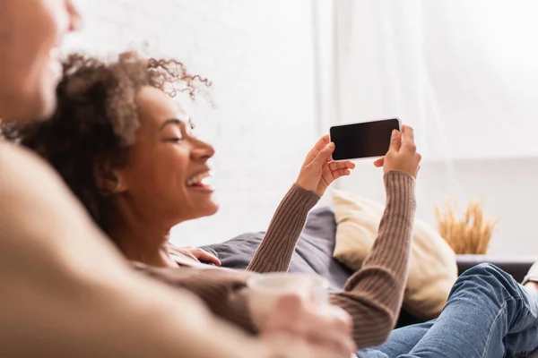 Smartphone with blank screen in hands of cheerful african american woman near boyfriend with cup at home — Stock Photo