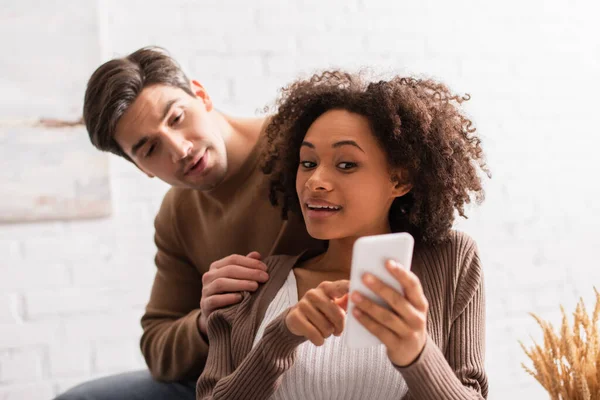 African american woman pointing at smartphone near boyfriend at home — Stock Photo