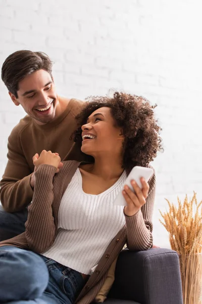 Positive african american woman holding cellphone and hand of boyfriend at home — Stock Photo