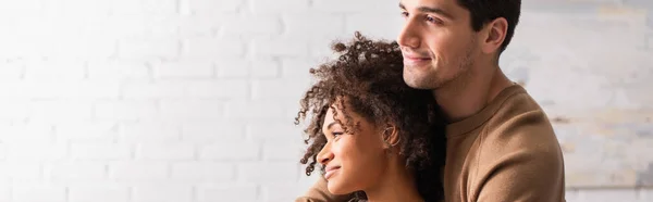 Hombre abrazando sonriente afro-americana novia en casa, bandera - foto de stock