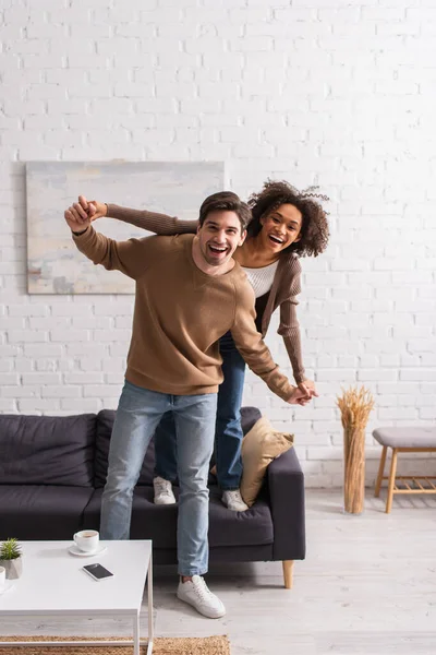 Positive interracial paar halten hände und schauen auf kamera zu hause — Stockfoto