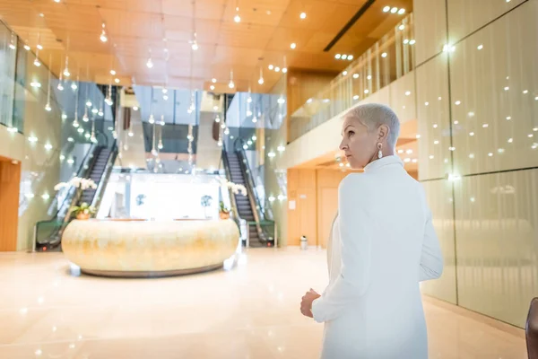 Mature and trendy businesswoman standing in spacious lobby of luxury hotel — Stock Photo