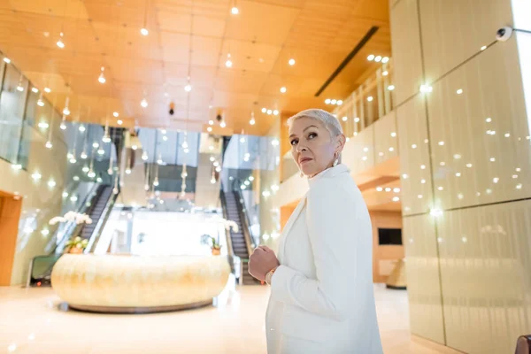 Matura donna d'affari guardando indietro mentre in piedi nella hall di hotel di lusso — Foto stock