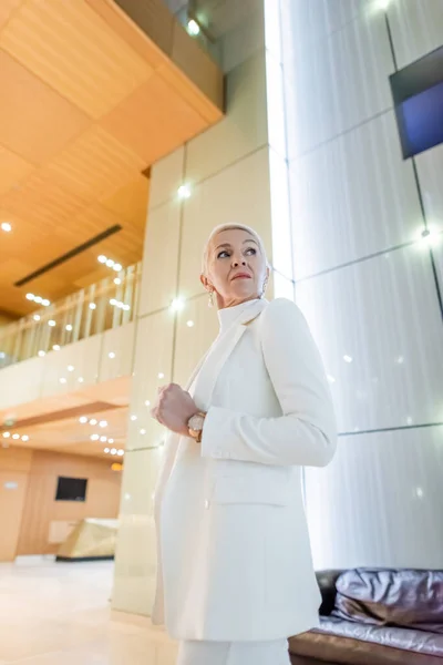 Blick auf eine wohlhabende Geschäftsfrau im weißen Blazer, die in einem modernen Hotel wegschaut — Stockfoto