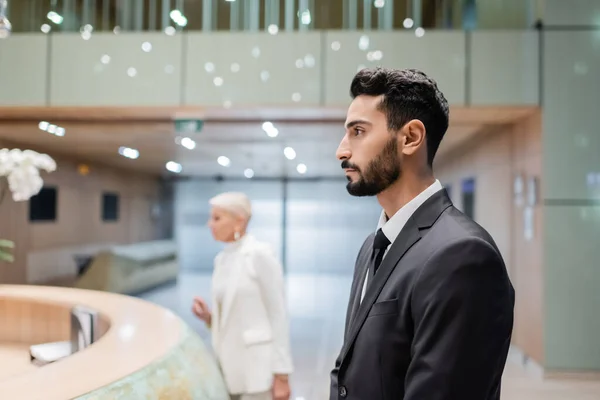 Vue latérale de l'homme de sécurité bi-raciale près floue femme d'affaires enregistrement à la réception de l'hôtel — Photo de stock