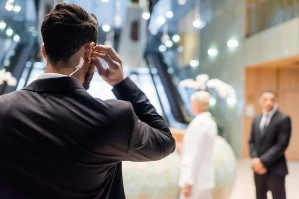 Vista posterior del hombre de seguridad bi-racial ajustando el auricular cerca de la mujer de negocios borrosa y el guardaespaldas afroamericano - foto de stock