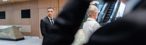 African american bodyguard escorting senior businesswoman in hotel hall on blurred foreground, banner — Stock Photo