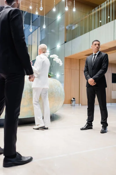 Interracial security men standing near senior businesswoman checking in at hotel reception — Stock Photo