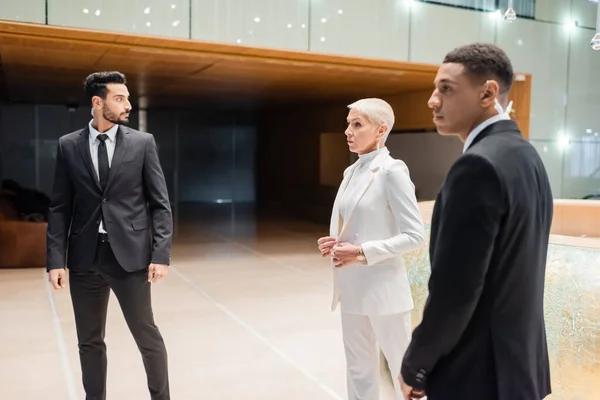 Interracial guards looking aside near mature businesswoman in hotel lobby — Stock Photo