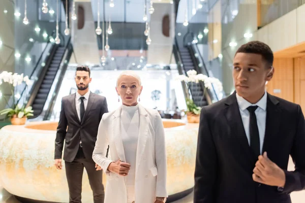Interracial security men escorting senior businesswoman in modern hotel — Stock Photo