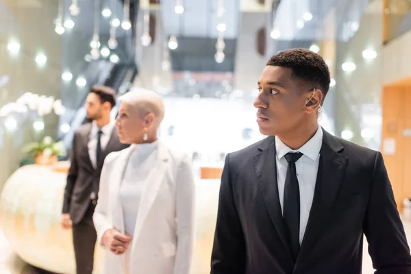 African american security man in earpiece looking away while escorting senior businesswoman in hotel — Stock Photo