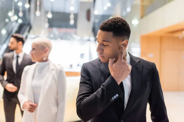 African american bodyguard adjusting earpiece near mature businesswoman with bi-racial guard on blurred background — Stock Photo