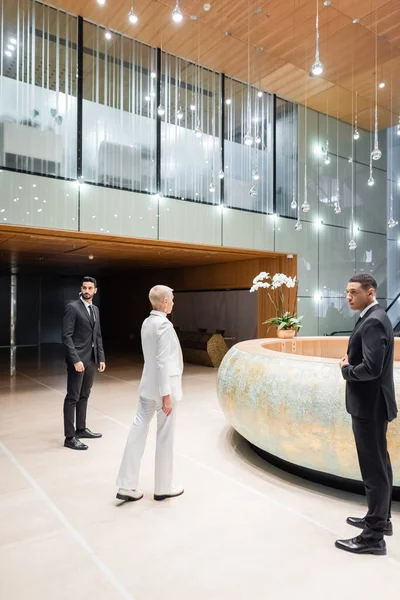 Multiethnic bodyguards near senior businesswoman walking towards hotel reception — Stock Photo