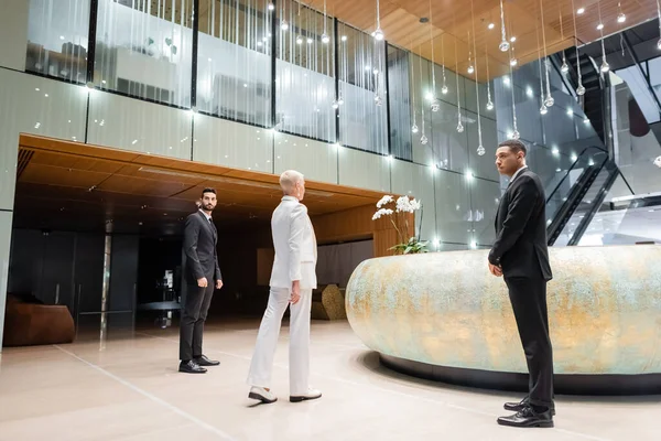 Piena lunghezza vista di uomini di sicurezza multiculturali vicino elegante donna d'affari a piedi nella hall dell'hotel — Foto stock