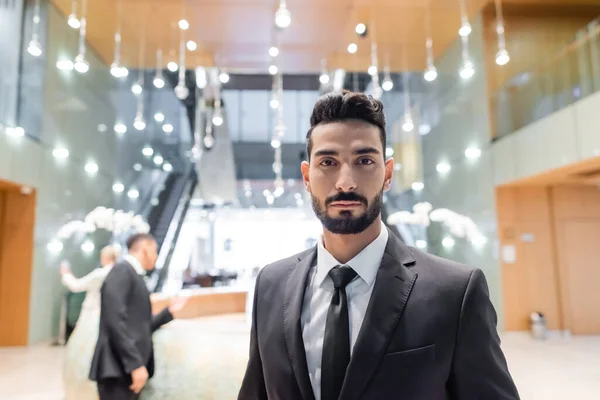 Junger, birassistischer Sicherheitsmann blickt in die Kamera in der Nähe einer Seniorin mit Leibwächter auf verschwommenem Hintergrund — Stockfoto