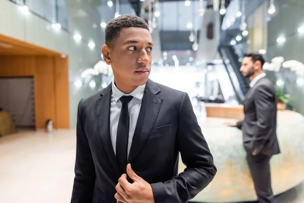 African american guard looking away in hotel lobby near mixed race colleague on blurred background — Stock Photo