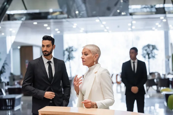 Interracial bodyguards protecting mature businesswoman standing at hotel reception — Stock Photo