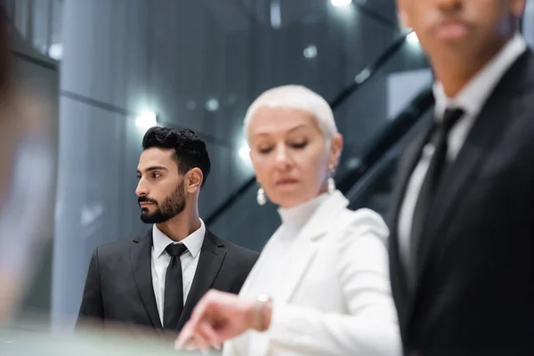 Homem de segurança bi-racial perto de empresária sênior verificando o tempo no hotel em primeiro plano turvo — Fotografia de Stock