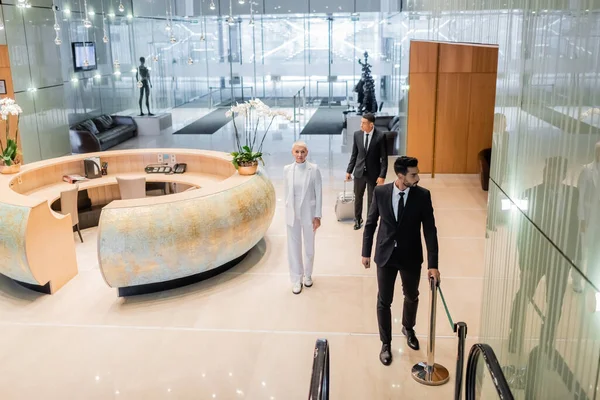 Vista de ángulo alto de guardaespaldas multiétnicos en desgaste formal escoltando a la dama de negocios senior en un hotel de lujo - foto de stock