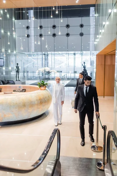 Multiethnic bodyguards in formal wear escorting trendy businesswoman in hotel hall — Stock Photo