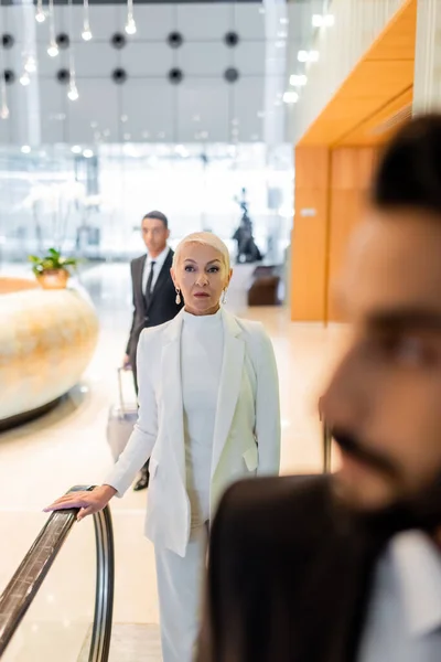 Enfoque selectivo de la mujer de negocios senior de moda cerca borrosa guardaespaldas multiétnicos en el hotel - foto de stock