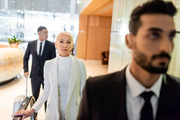 Interracial bodyguards protecting senior businesswoman in hotel foyer during business trip — Stock Photo