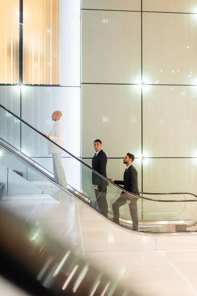 Senior femme d'affaires près de gardes du corps privés en tenue formelle sur l'escalier roulant de l'hôtel — Photo de stock