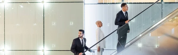 Trendy senior businesswoman near private interracial bodyguards on hotel escalator, banner — Stock Photo