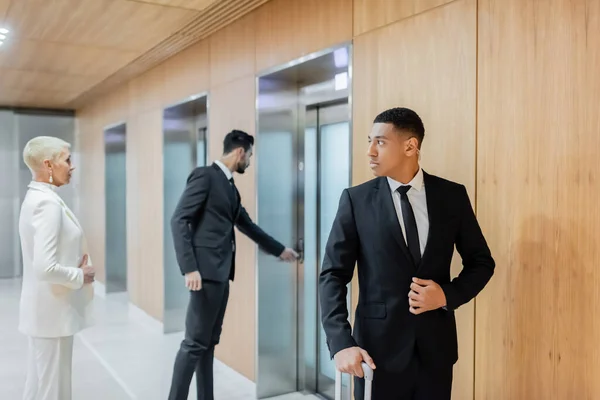 Interracial bodyguards escorting senior businesswoman near elevators in hotel — Stock Photo