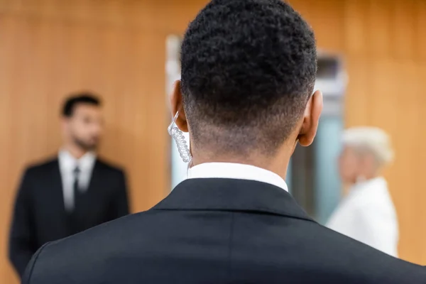 Rückansicht eines afrikanisch-amerikanischen Sicherheitsmannes in der Nähe einer verschwommenen Seniorin mit Leibwächter auf verschwommenem Hintergrund — Stockfoto