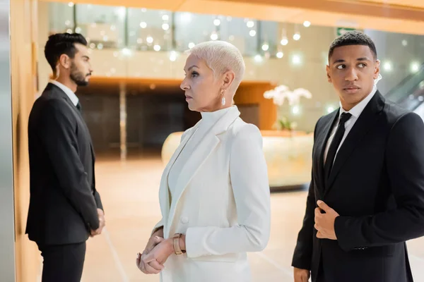 Multiethnic guards escorting senior businesswoman in hotel foyer during business trip — Stock Photo