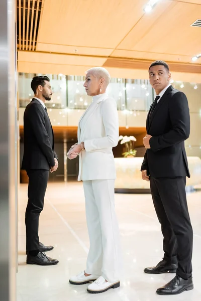 Full length view of wealthy businesswoman near private interracial bodyguards in hotel — Stock Photo