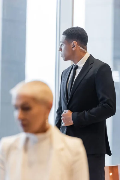 Hombre de seguridad afroamericano en auricular cerca de la mujer de negocios senior en primer plano borrosa - foto de stock