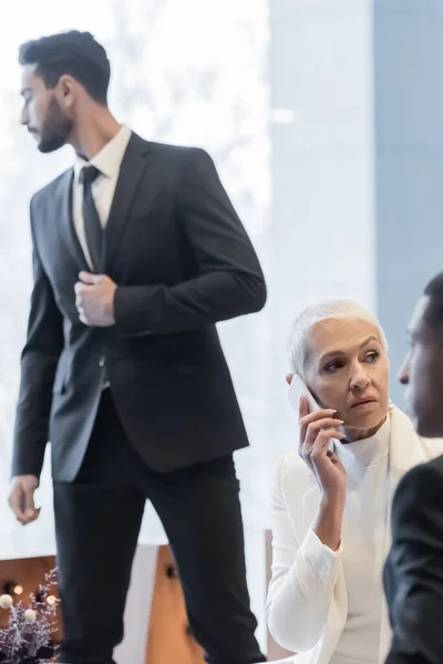 Femme d'affaires âgée parlant sur téléphone portable près floue hommes de sécurité multiethnique — Photo de stock