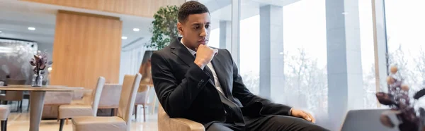 Serious and pensive african american security man sitting in hotel lounge, banner — Stock Photo