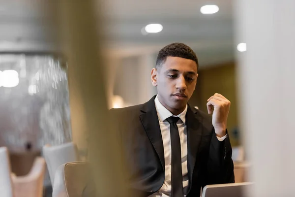Pensive african american man in suit sitting in hotel lobby on blurred foreground — Stock Photo