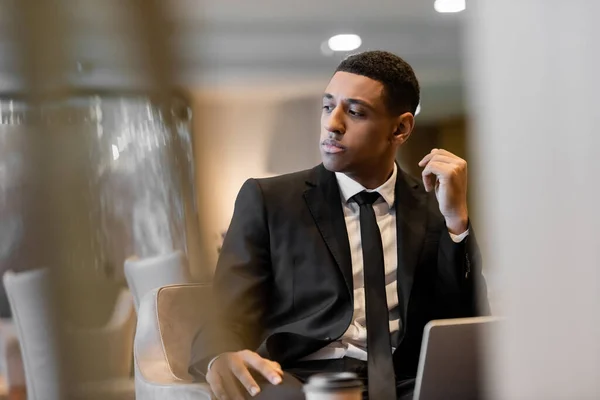 Pensativo guarda afro-americano sentado no salão do hotel em primeiro plano turvo — Fotografia de Stock