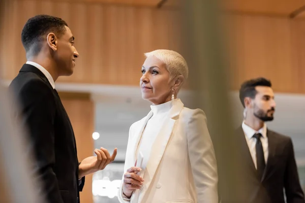 Homem de segurança afro-americano positivo falando com mulher de negócios sênior elegante perto de guarda-costas de raça mista — Fotografia de Stock