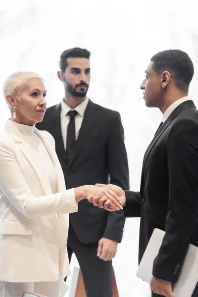 Élégante femme d'affaires senior serrant la main avec l'homme de sécurité afro-américain près mixte garde du corps race à l'hôtel — Photo de stock