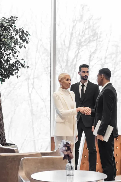 Senior businesswoman shaking hands with african american security man near bi-racial bodyguard in hotel — Stock Photo