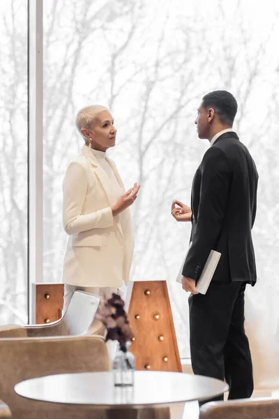 African american security man with laptop talking with senior business lady in hotel lounge — Stock Photo