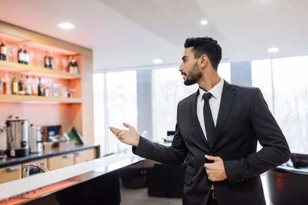 Junger Mischlingswächter zeigt mit der Hand in der Nähe einer verschwommenen Lobby-Bar — Stockfoto