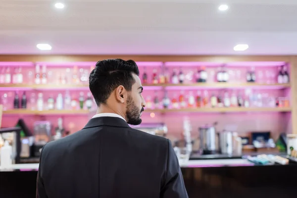 Vista trasera del hombre de seguridad bi-racial en blazer negro cerca del bar del vestíbulo borroso en el hotel - foto de stock