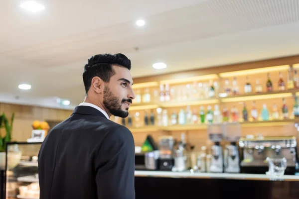 Giovane guardia di razza mista sorridente vicino al bar della hall offuscata in hotel — Foto stock