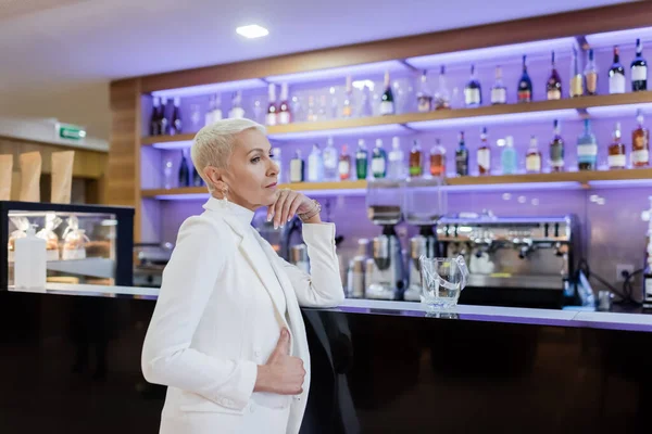 Femme d'affaires mature en blazer blanc debout au comptoir du bar dans le hall de l'hôtel — Photo de stock