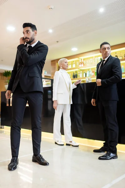 Vista completa de guardaespaldas multiculturales y dama de negocios de moda en el bar del vestíbulo en el hotel - foto de stock